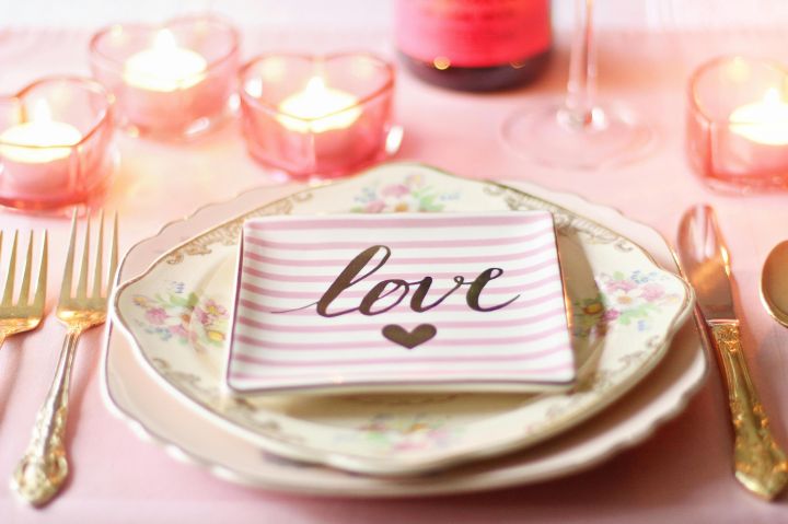 Elegant romantic dinner setup with heart-shaped candles and 'love' plate.