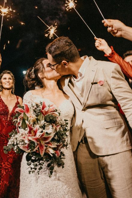 A joyful couple kisses under sparklers, surrounded by guests in a wedding celebration.