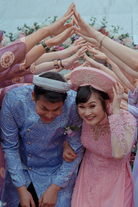 Happy Vietnamese couple celebrates their wedding with friends in traditional attire outdoors.